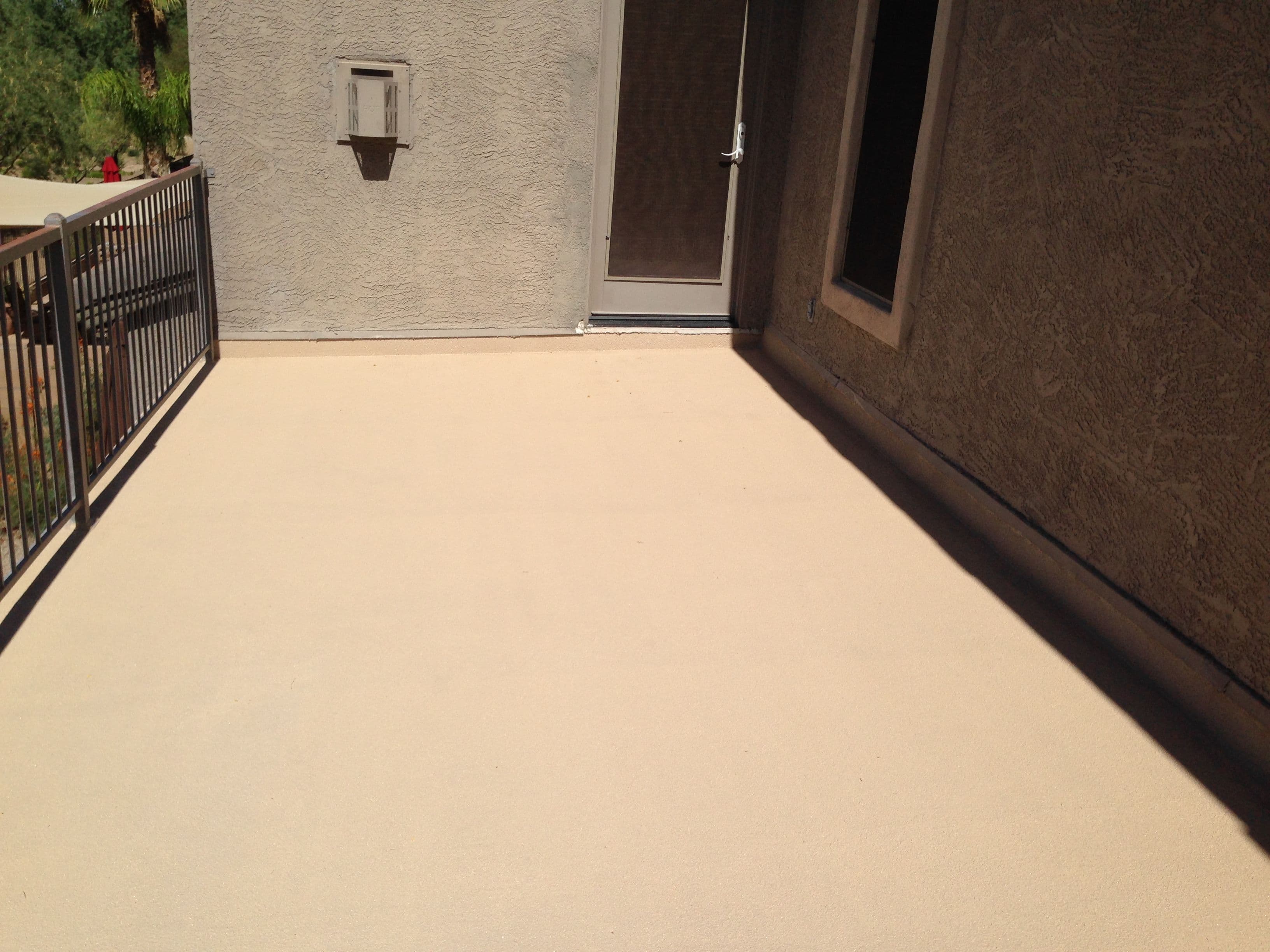 Clean, dry patio surface with a railing and door against a textured wall.