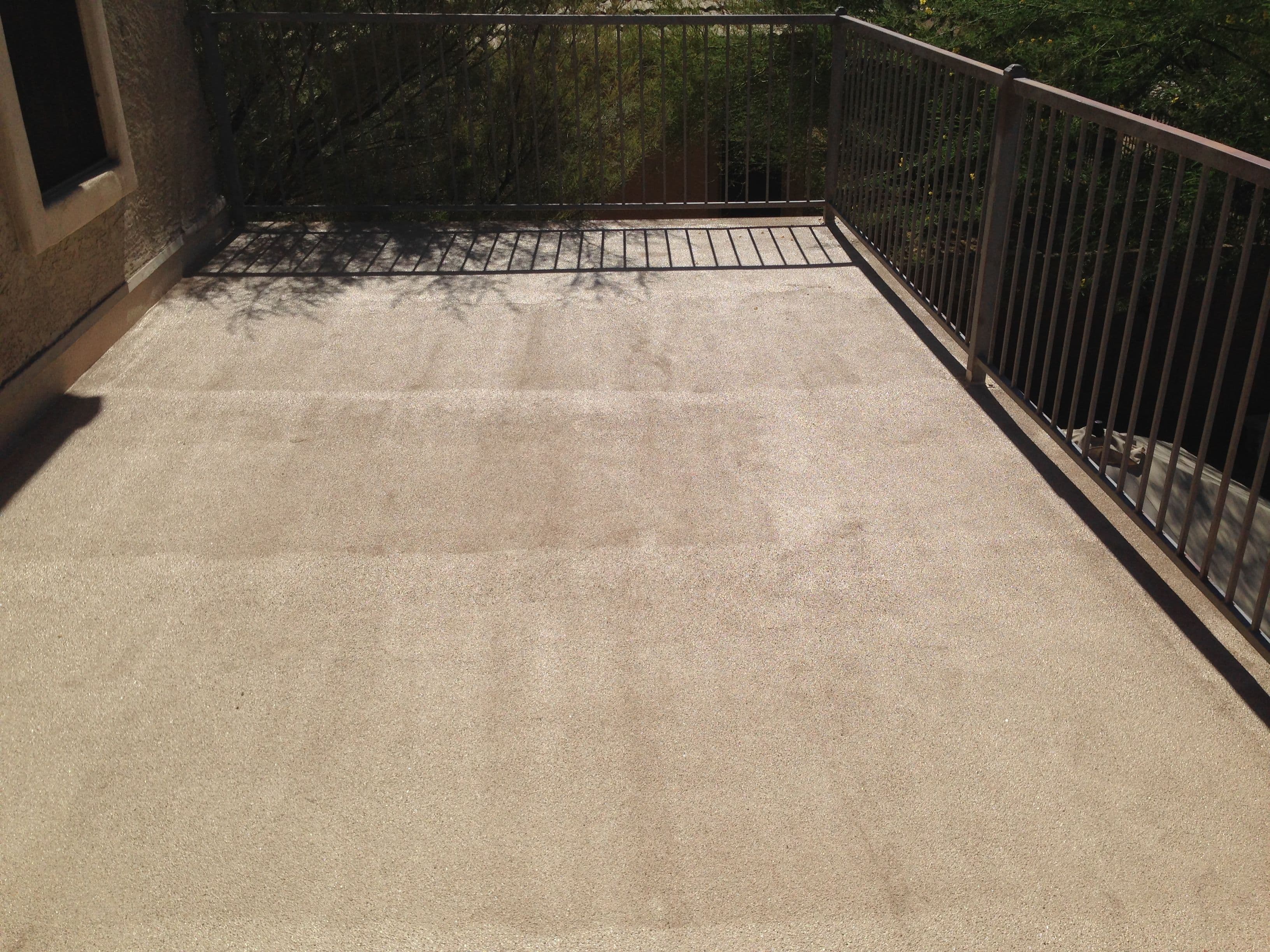 Empty outdoor patio with a smooth, light-colored surface and metal railing under sunlight.